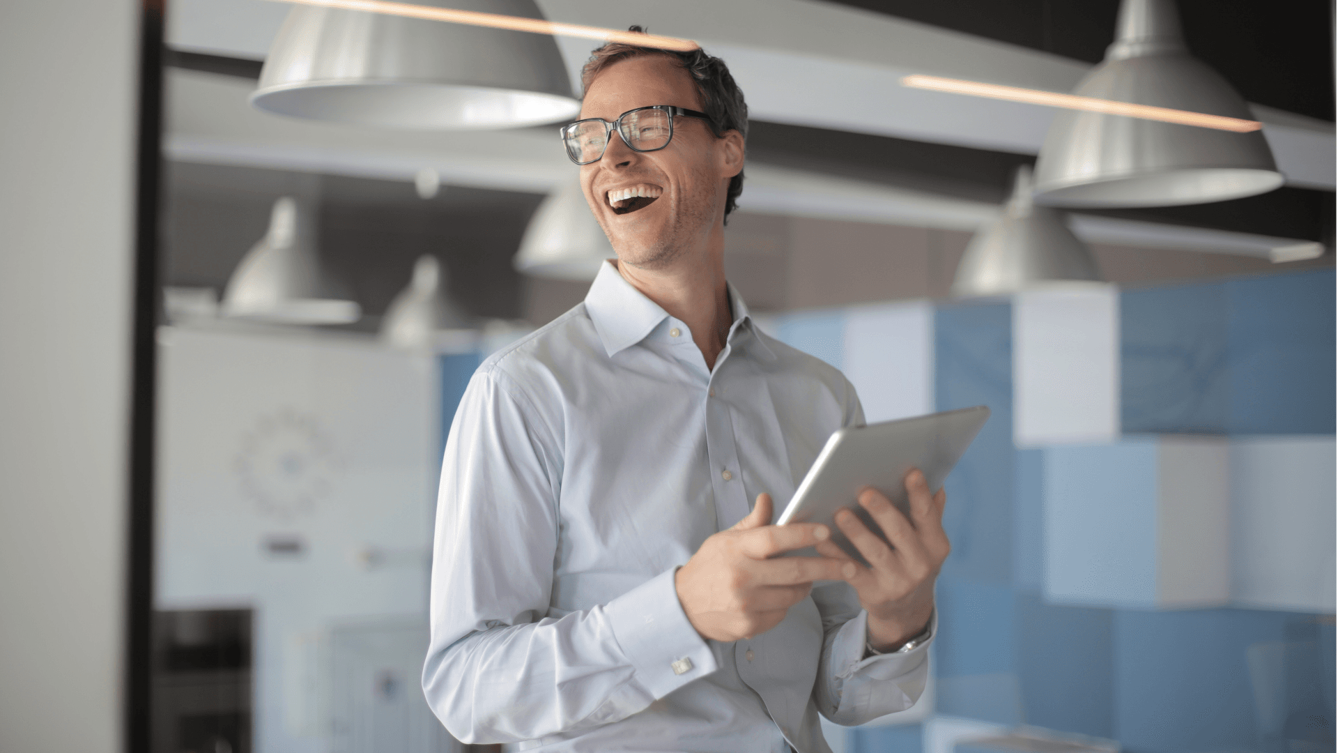 Man standing and holding a tablet laughing
