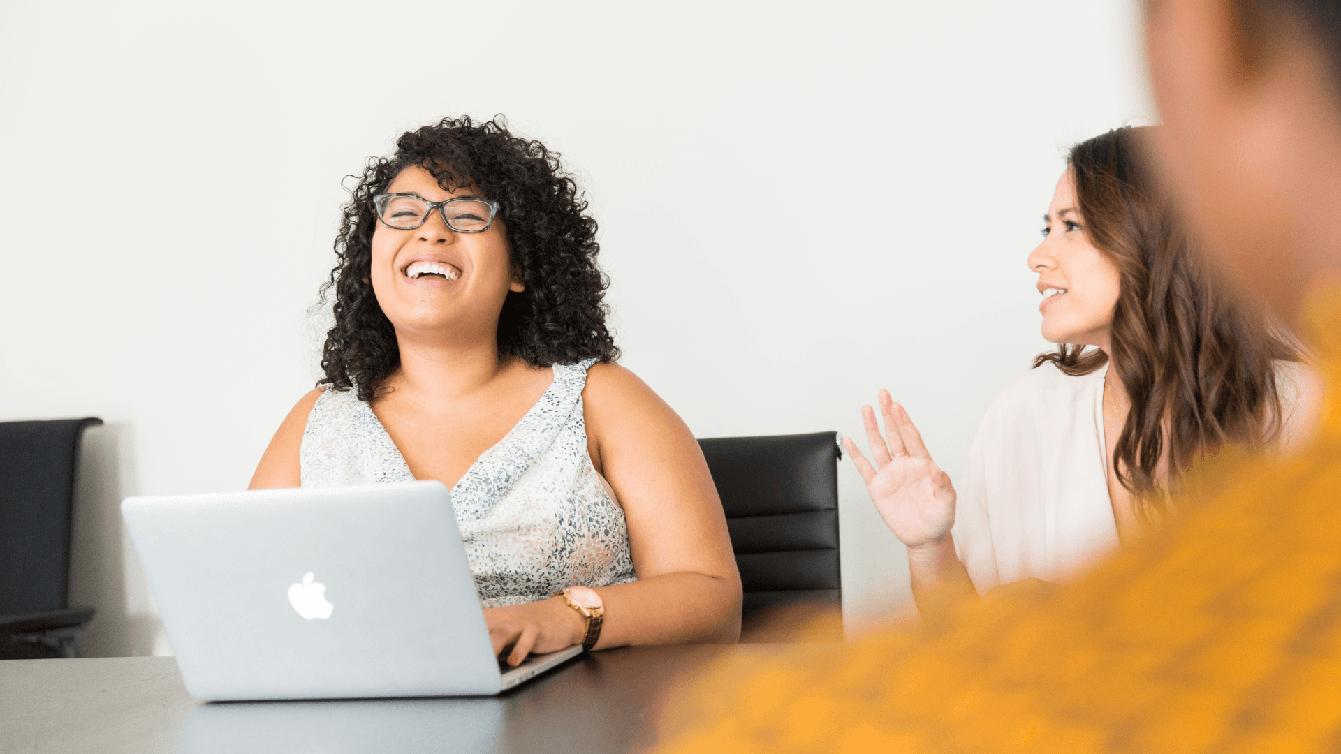 Woman in a meeting sitting at a table with her laptop and laughing