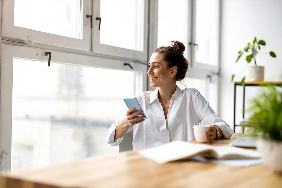 woman in white shirt, holding a mobile phone and a cup