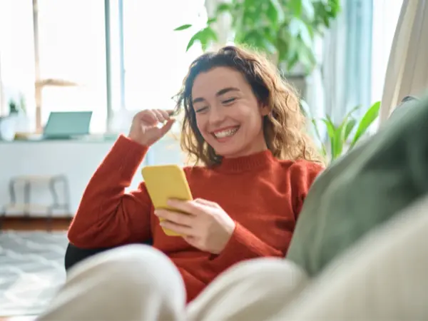 Nainen makoilee sohvalla ja katsoo puhelinta